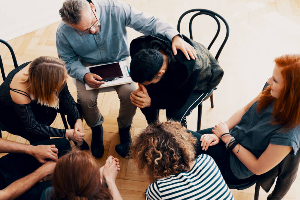 High-End Rehab California 1 Troubled man consoling by his group members in a group session in rehab center