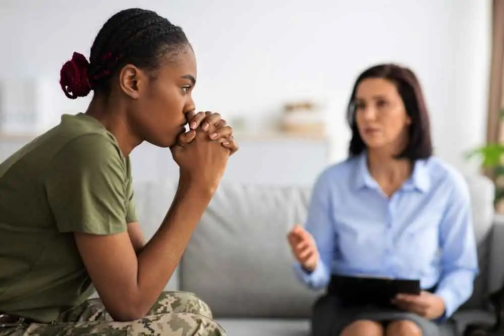 woman in a green shirt and camouflage trousers speaking with a counselor