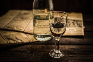 A shot glass of transparent vodka stands beside a vodka bottle on a textured wooden table, illustrates the question, does vodka expire