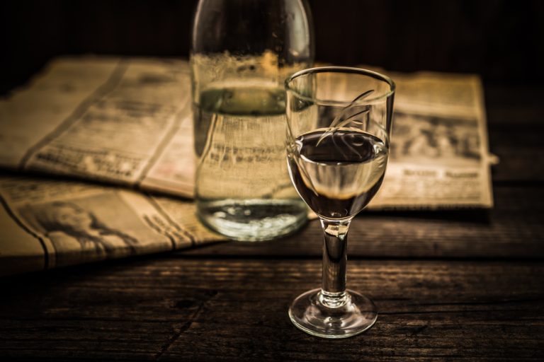 a shot glass of transparent vodka stands beside a vodka bottle on a textured wooden table, illustrates the question, does vodka expire