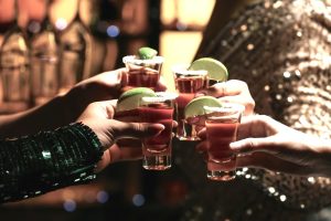 Hands holding five tequila shots with lime, suggesting how many shots can get you drunk in a party setting