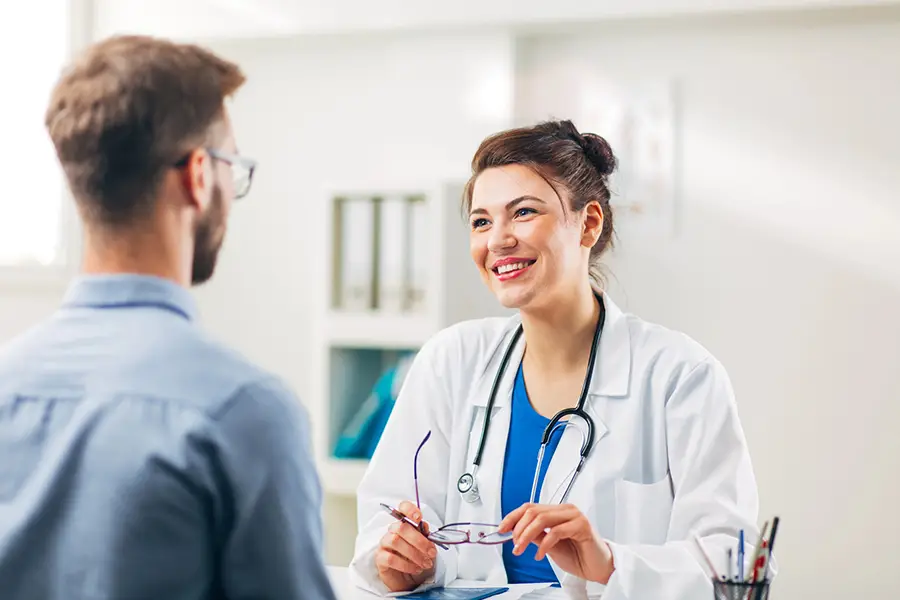 A female doctor smiles while consulting with a male patient, discussing opioid withdrawal treatment monitoring in an office