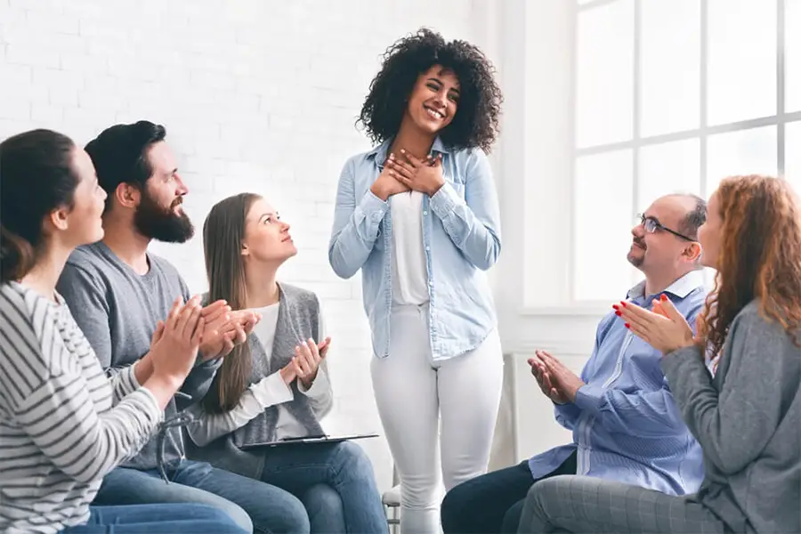 A group claps for a smiling woman at a support meeting, symbolizing success in opioid detox monitoring