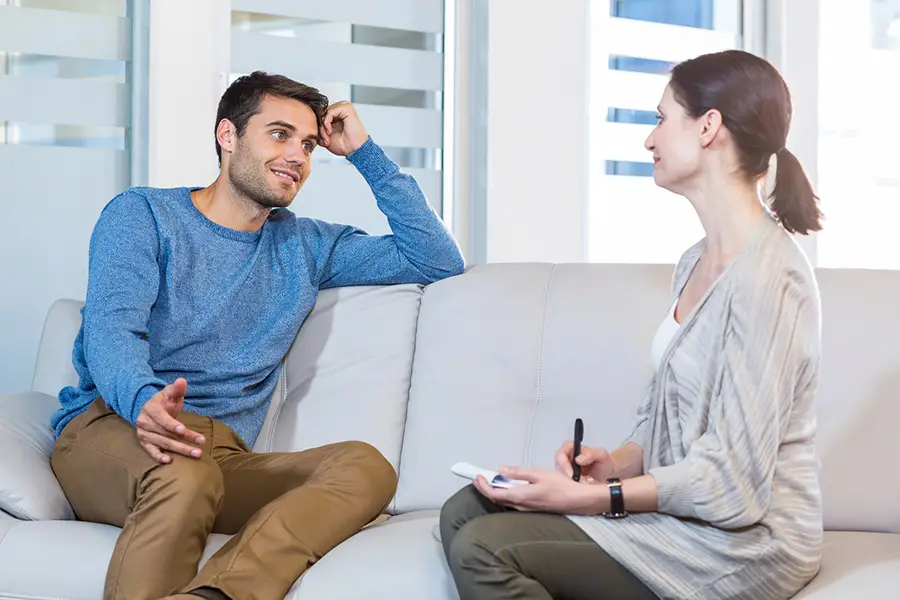 A man in a therapy session, representing what to expect in rehab, talking with a female therapist taking notes.
