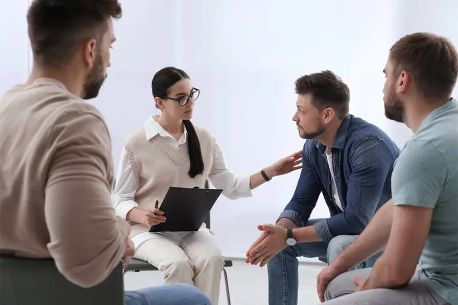 Group therapy session showing what happens during rehab, with a therapist comforting a male patient.