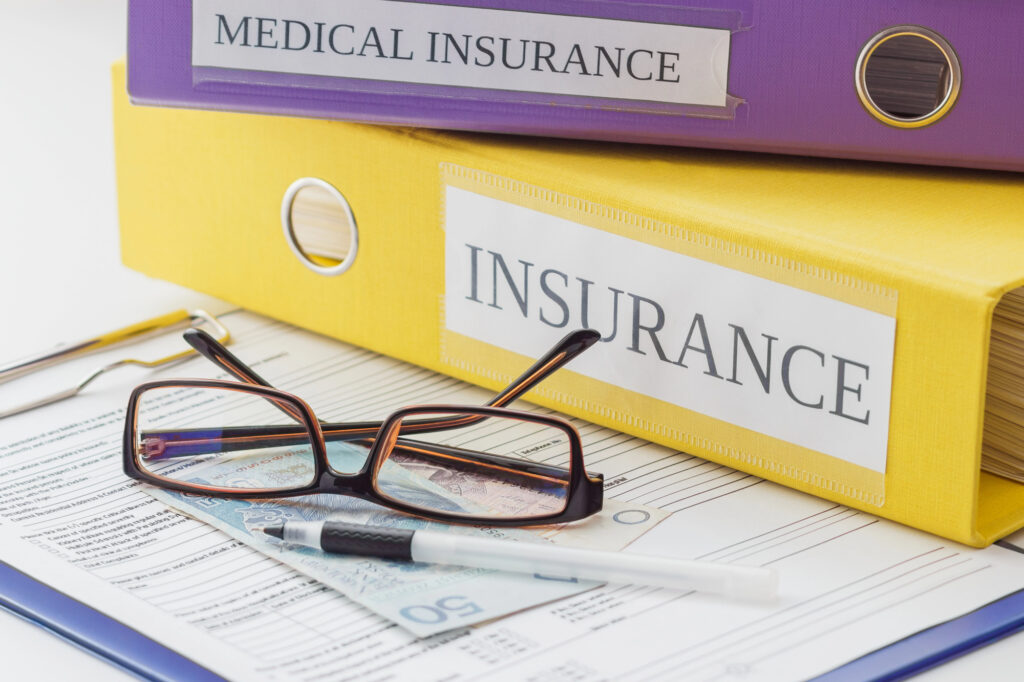 notebooks about medical insurance policy sit on top of paperwork while someone files for insurance verification for rehab