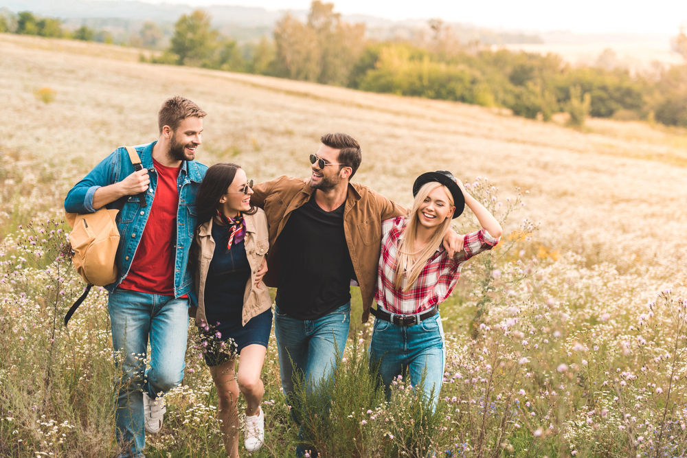 four young adults walk together in a sunny field, smiling and supporting each other, representing an aftercare support group for heroin addiction.