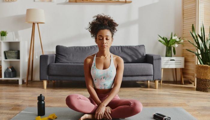 4 Reasons Why Self-Care is Key During National Substance Abuse Prevention Month A woman in activewear suffering from substance abuse practicing yoga on a mat in a cozy living room setting