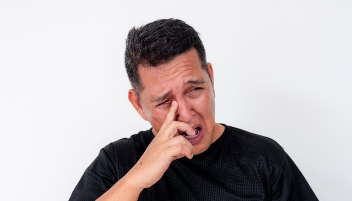 5 Signs of Cocaine Eyes A man in black shirt removing eye discharge from his tear duct.
