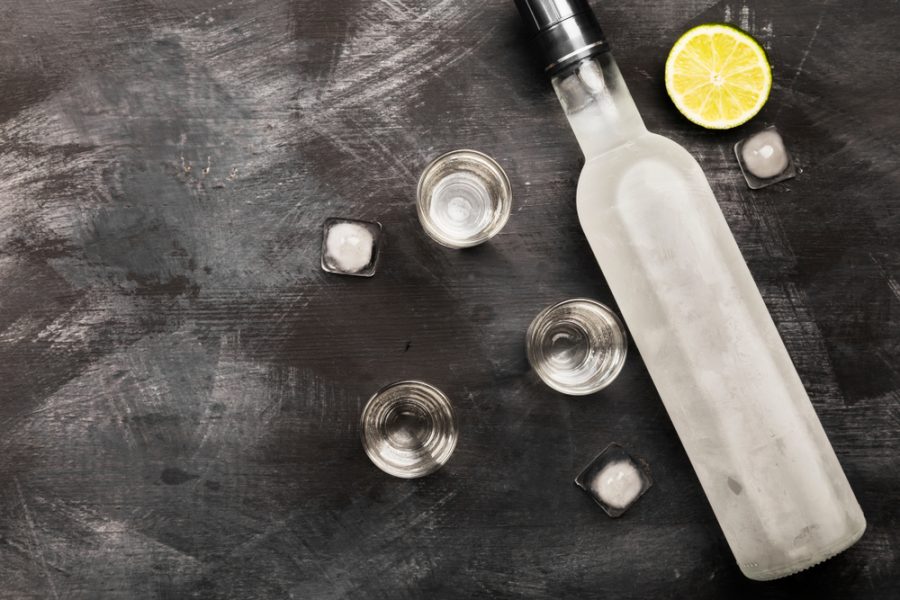 Frosted vodka bottle with shot glasses, lime, and ice cubes on a dark table, illustrating vodka shelf life Frosted vodka bottle with shot glasses, lime, and ice cubes on a dark table, illustrating vodka shelf life