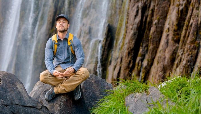 a man meditating while sitting on a big stone