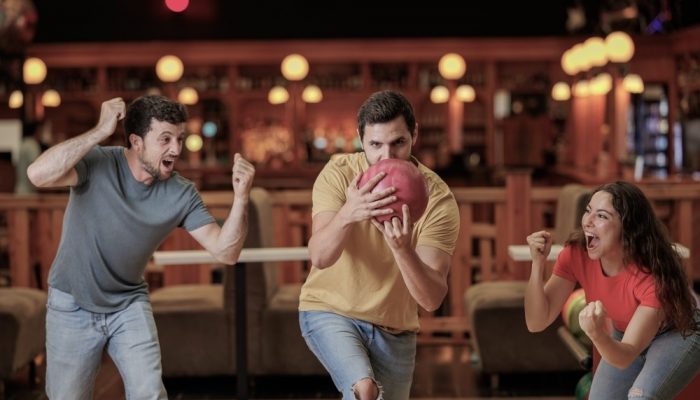 group of sober amd happy young friends having fun and cheering while playing bowling game
